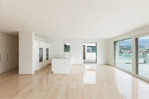 Empty modern living room with large windows and polished wooden flooring, illustrating a spacious environment ideal for energy-efficient HVAC settings.