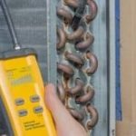 Technician measuring HVAC coil with yellow device, showcasing copper tubing and fins for Easco Air Conditioning.