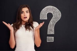 Woman looking surprised with raised hands beside a large chalkboard question mark, symbolizing inquiries about air sanitizers and purifiers.