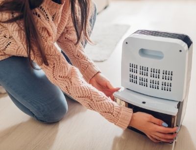 Person operating a dehumidifier, demonstrating maintenance by removing the water collection tank, emphasizing home humidity control and air quality improvement.