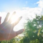 Hand reaching toward sun rays with trees and blue sky in the background, reflecting Easco Air Conditioning services.