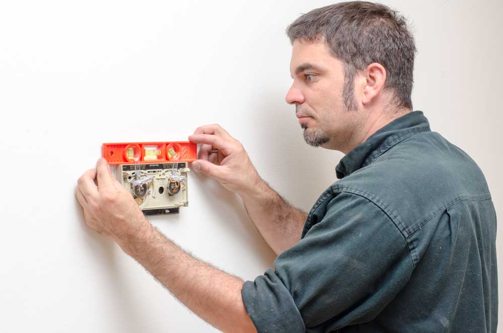 Technician installing a thermostat using a level tool, emphasizing HVAC maintenance and service expertise.