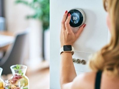 Person adjusting a smart thermostat to optimize home cooling and reduce energy costs, with drinks visible in the foreground, illustrating HVAC efficiency tips.