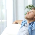 Man seated on a chair in natural light, showing a relaxed demeanor, representing comfort in energy-efficient HVAC solutions.