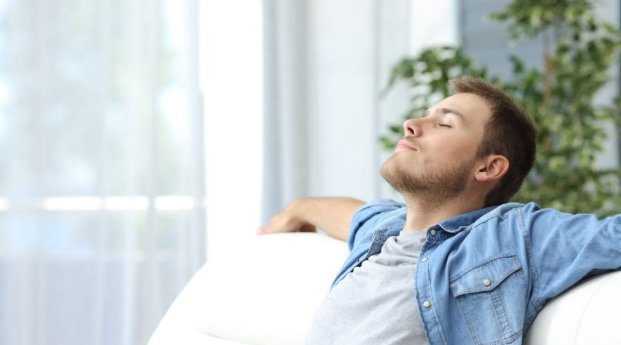 Young man on a white couch in a cozy indoor setting, showcasing energy-efficient HVAC solutions by Easco Air Conditioning.