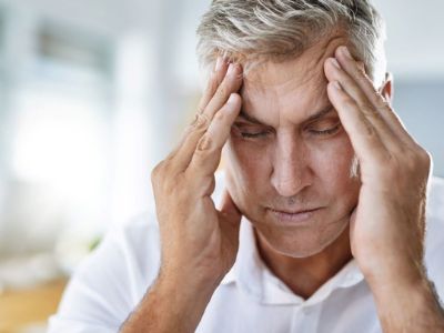 Man with gray hair holding his head in discomfort, illustrating the health effects of poor indoor air quality on respiratory health.