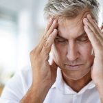 Male HVAC technician with gray hair in distress, hands on forehead in an office, emphasizing energy-efficient solutions.