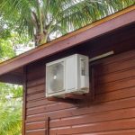 Air conditioning unit on a wooden wall amid palm trees, showcasing HVAC efficiency by Easco.