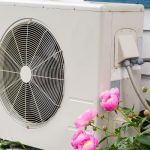 Air conditioning unit with ventilation grille and pink peonies, showcasing energy-efficient HVAC solutions.