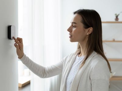 A woman adjusting a smart thermostat in a minimalist room to enhance HVAC efficiency and comfort.