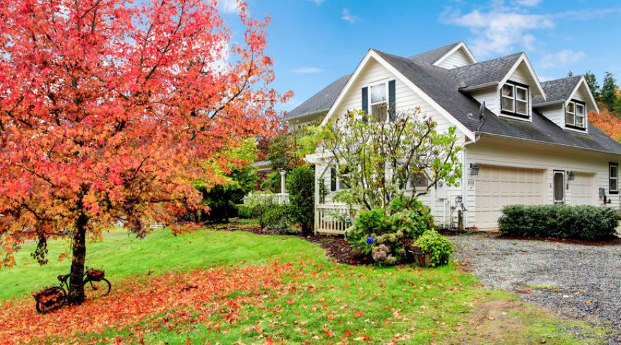 Fall landscape with a vibrant red tree and a charming home, highlighting seasonal changes and the importance of preparing HVAC systems for cooler temperatures.