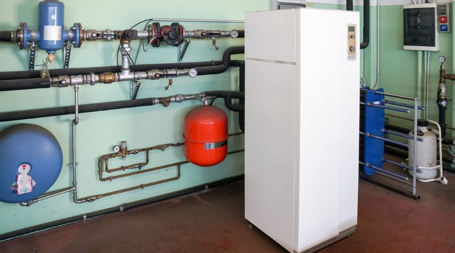 White refrigerator among plumbing pipes and gauges, representing HVAC services for indoor air quality in Conroe, TX.