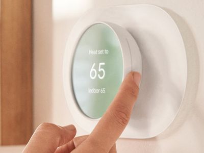Hand adjusting a smart thermostat displaying "Heat set to 65" for optimizing indoor temperature and energy efficiency in HVAC systems.