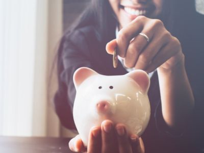 Woman smiling while inserting a coin into a white piggy bank, symbolizing savings and financial management.