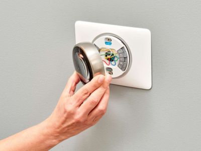 Hand installing a smart thermostat on a wall, showcasing wiring connections and modern design, emphasizing energy efficiency and home comfort.