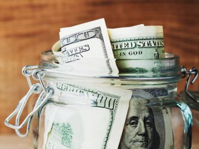 Jar filled with U.S. dollar bills, symbolizing savings from efficient air conditioner maintenance and reduced cooling costs.
