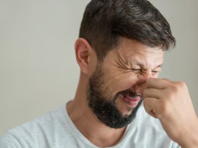 Man grimacing while pinching his nose, indicating discomfort possibly due to unusual odors from a heating system, relevant to heater maintenance and efficiency concerns.