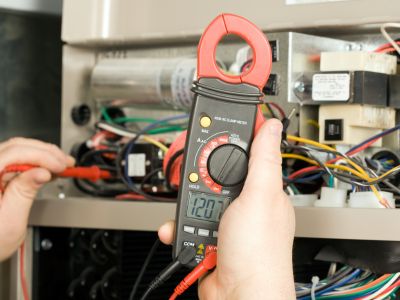 Electric multimeter being used for furnace maintenance and troubleshooting electrical issues in HVAC systems.